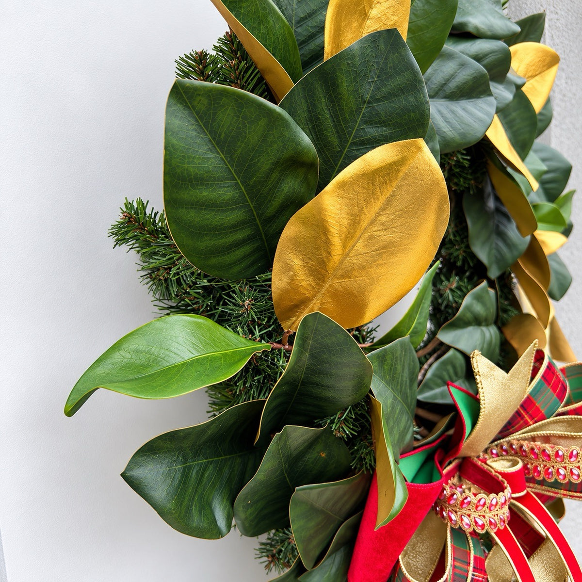 Handmade magnolia Christmas wreath with gold leaves and oversized red green tartan plaid and jeweled holiday bow