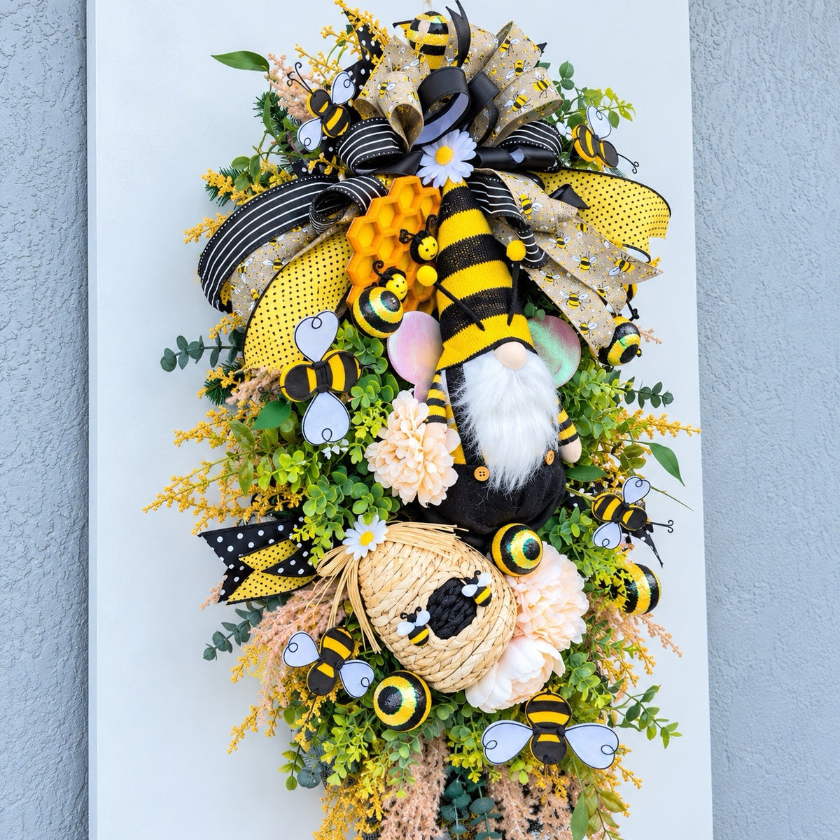 Handmade Queen Bee Manor wreath featuring a bee gnome, woven beehive, yellow and black designer bow, honeycomb accents, florals, bees, and lush greenery.
