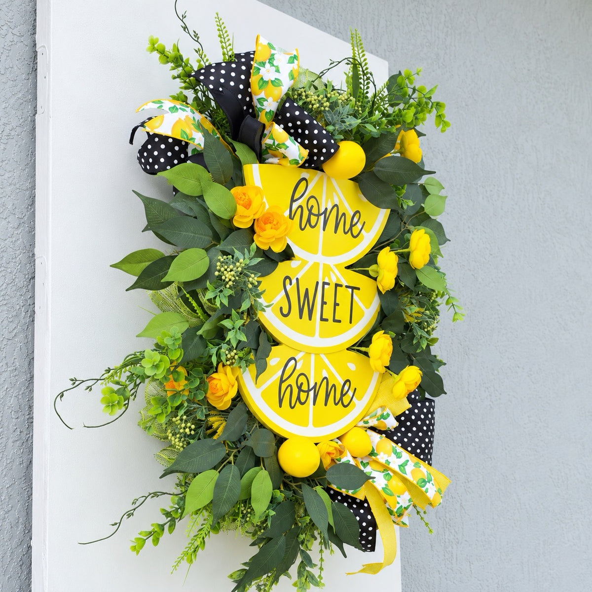 Handmade Lemon Sweet Home Summer Wreath featuring a yellow lemon-slice Home Sweet Home sign, bright yellow roses, decorative lemons, lush green foliage, and black-and-white polka-dot ribbon displayed on a white door.