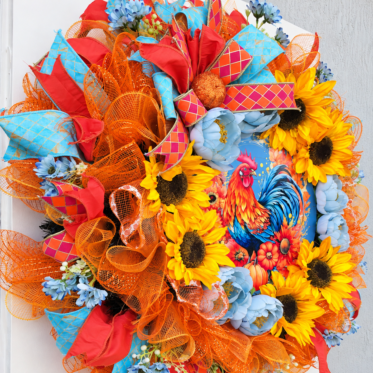 Handmade fall rooster wreath featuring vibrant yellow sunflowers, dusty blue flowers, orange deco mesh, coral and turquoise ribbons, and a colorful rooster centerpiece. A full farmhouse-style autumn wreath displayed on a white front door.