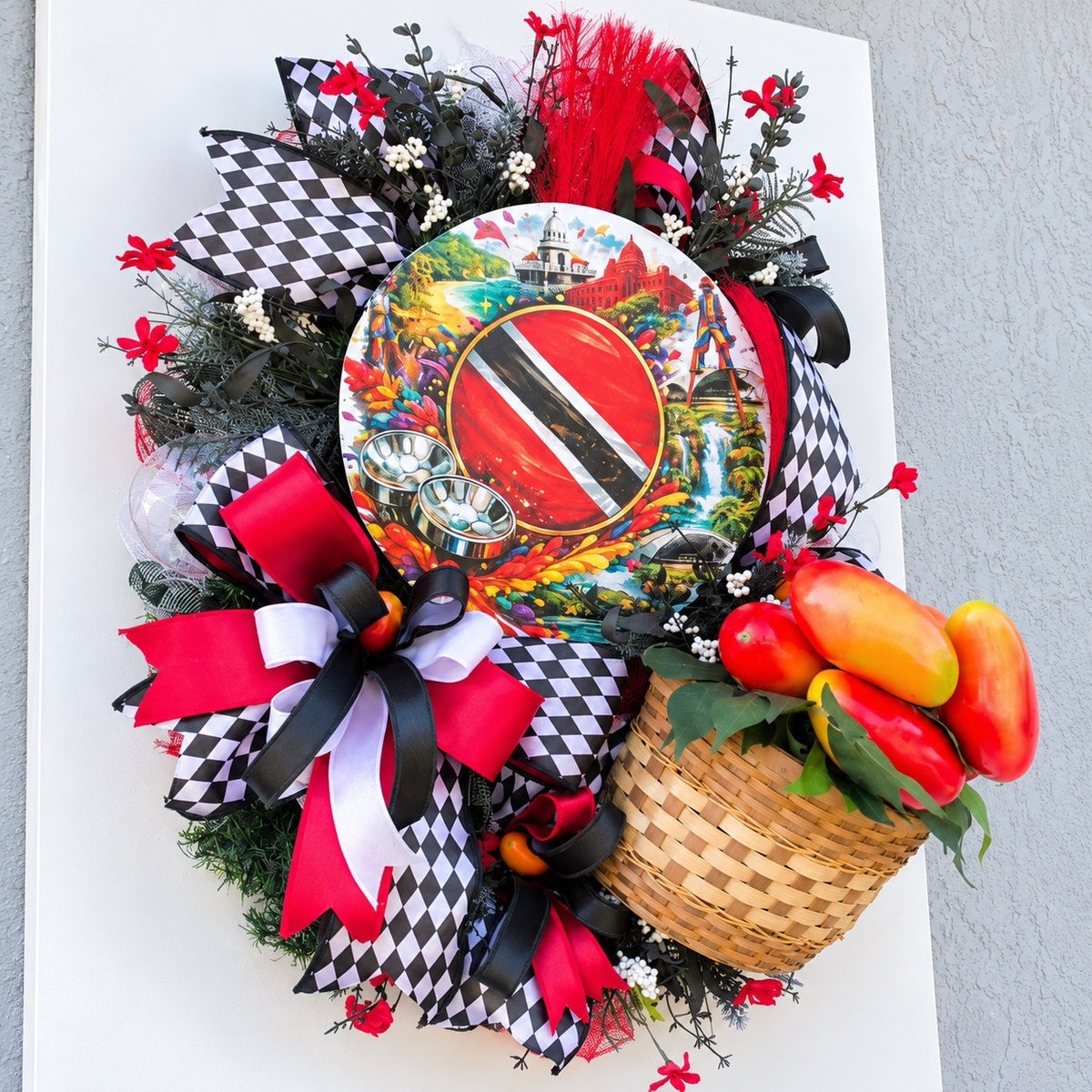 Angled left view of handmade Trinidad and Tobago wreath showing layered harlequin ribbons, red decorative accents, tropical greenery and cultural centerpiece sign.
