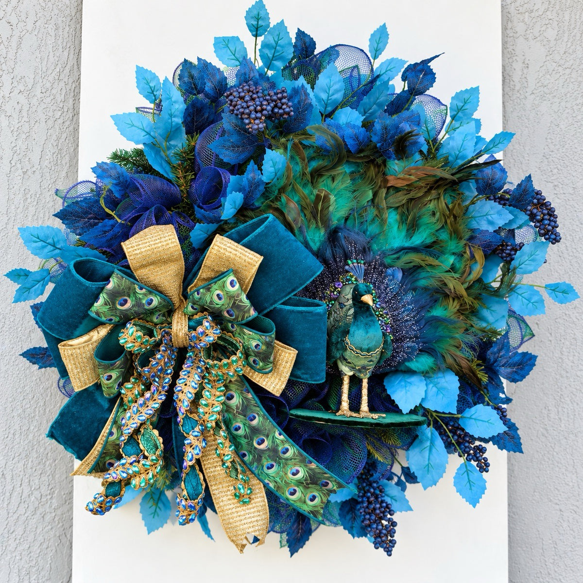 Left-angle view of handmade peacock wreath showing dimensional blue foliage and decorative ribbon.