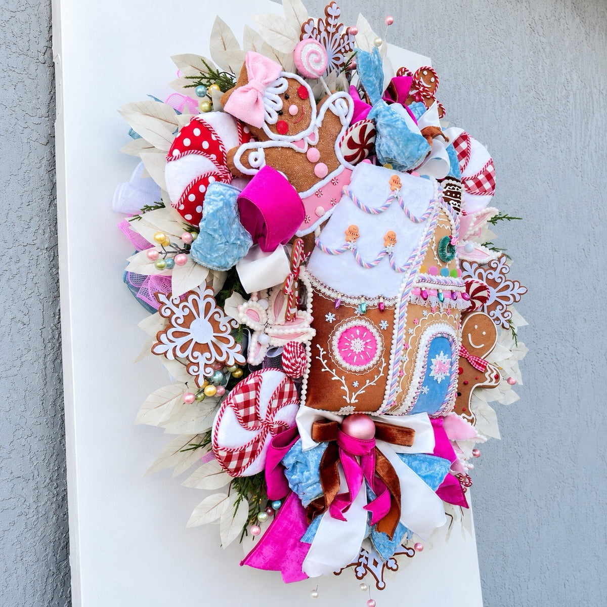 Sugarplum Gingerbread Cottage Christmas Wreath with pastel gingerbread house, pink and blue bows, poinsettias and Norfolk fir greenery.