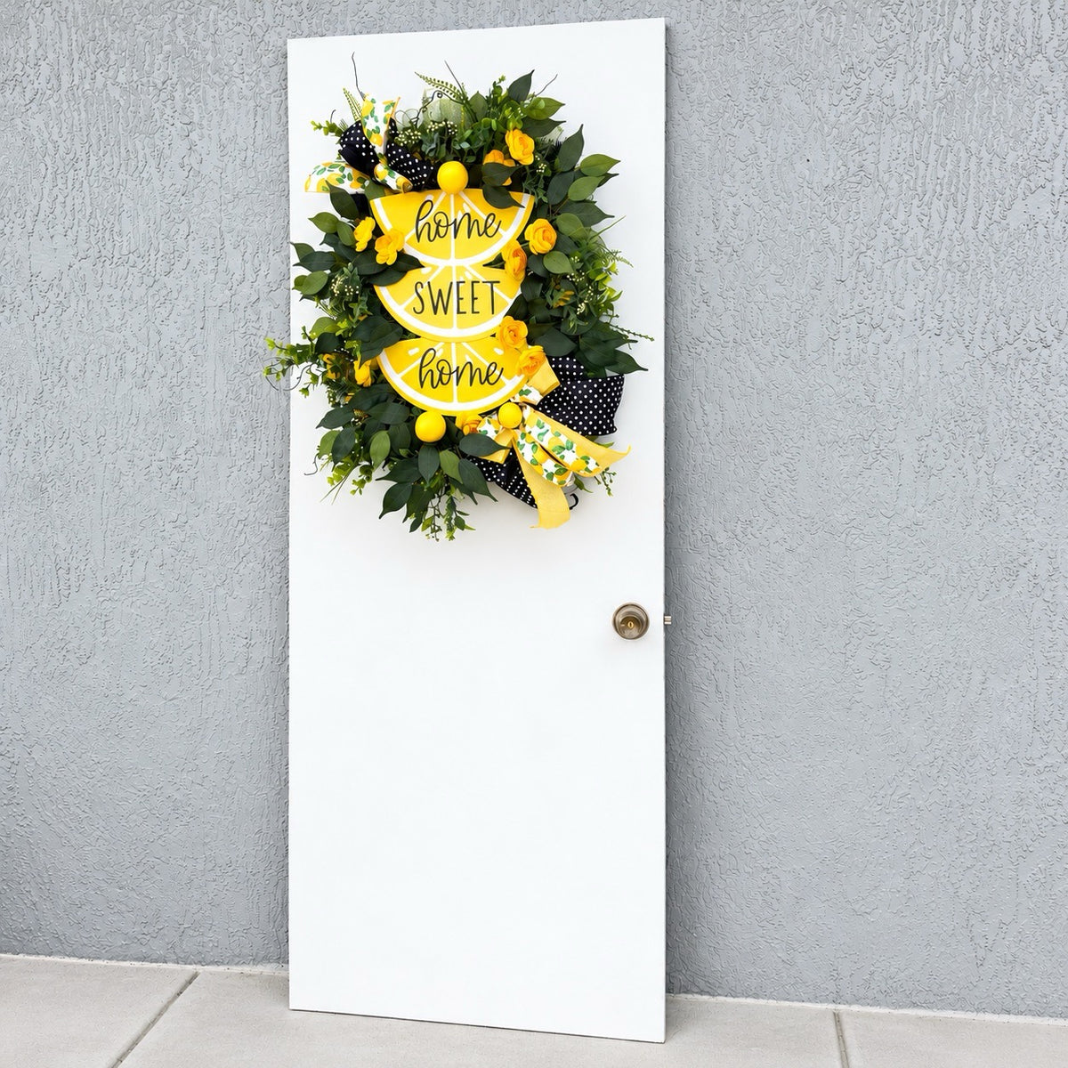 Handmade Lemon Sweet Home Summer Wreath featuring a yellow lemon-slice Home Sweet Home sign, bright yellow roses, decorative lemons, lush green foliage, and black-and-white polka-dot ribbon displayed on a white door.