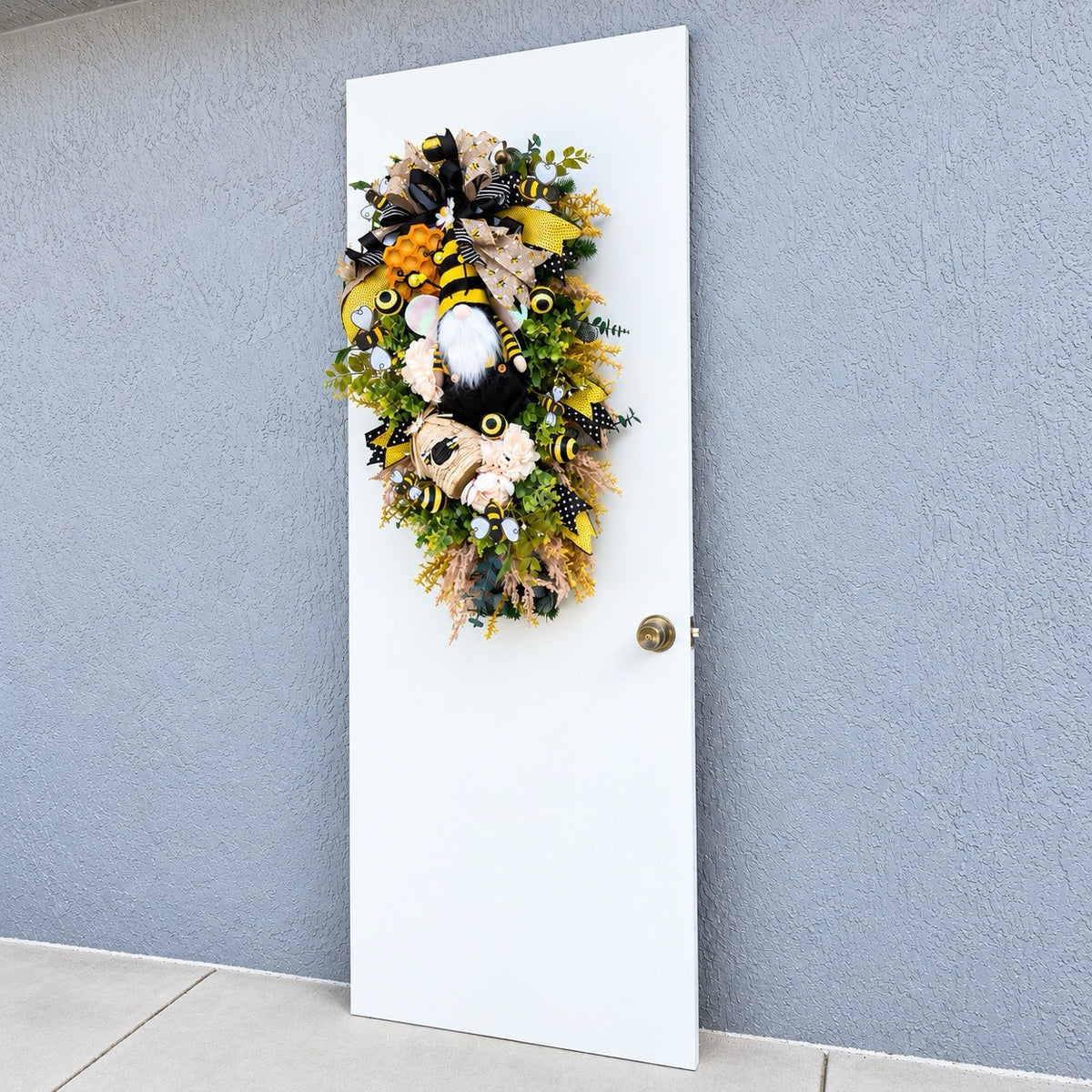 Handmade Queen Bee Manor wreath featuring a bee gnome, woven beehive, yellow and black designer bow, honeycomb accents, florals, bees, and lush greenery.