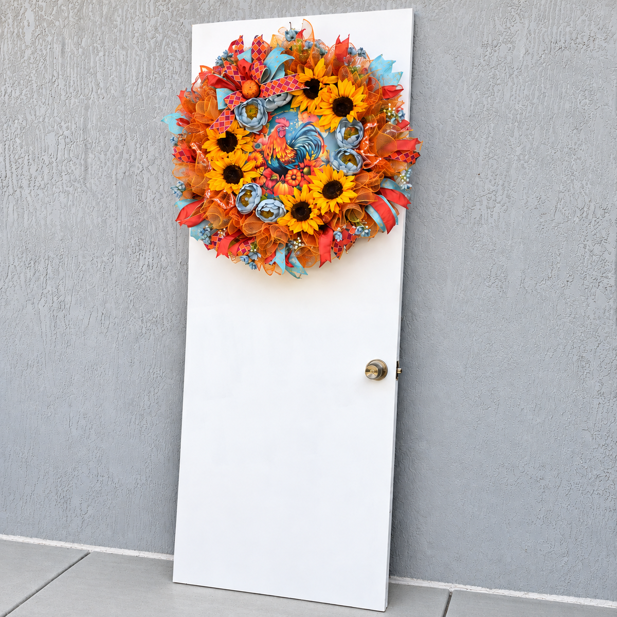 Handmade fall rooster wreath featuring vibrant yellow sunflowers, dusty blue flowers, orange deco mesh, coral and turquoise ribbons, and a colorful rooster centerpiece. A full farmhouse-style autumn wreath displayed on a white front door.