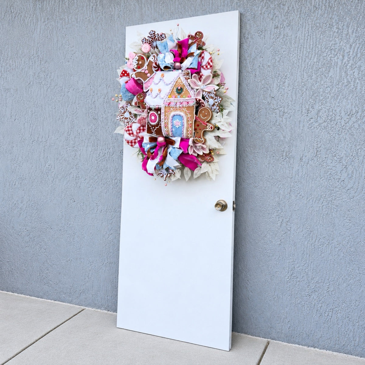 Sugarplum Gingerbread Cottage Christmas Wreath with pastel gingerbread house, pink and blue bows, poinsettias and Norfolk fir greenery.