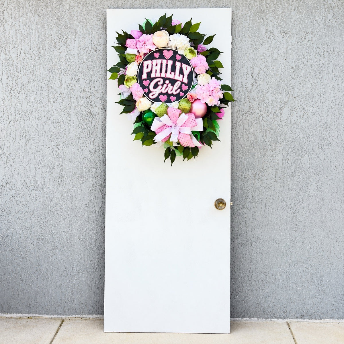 Philly Girl pink and green floral wreath displayed on a white front door with colorful flowers and a Philadelphia-inspired centerpiece.