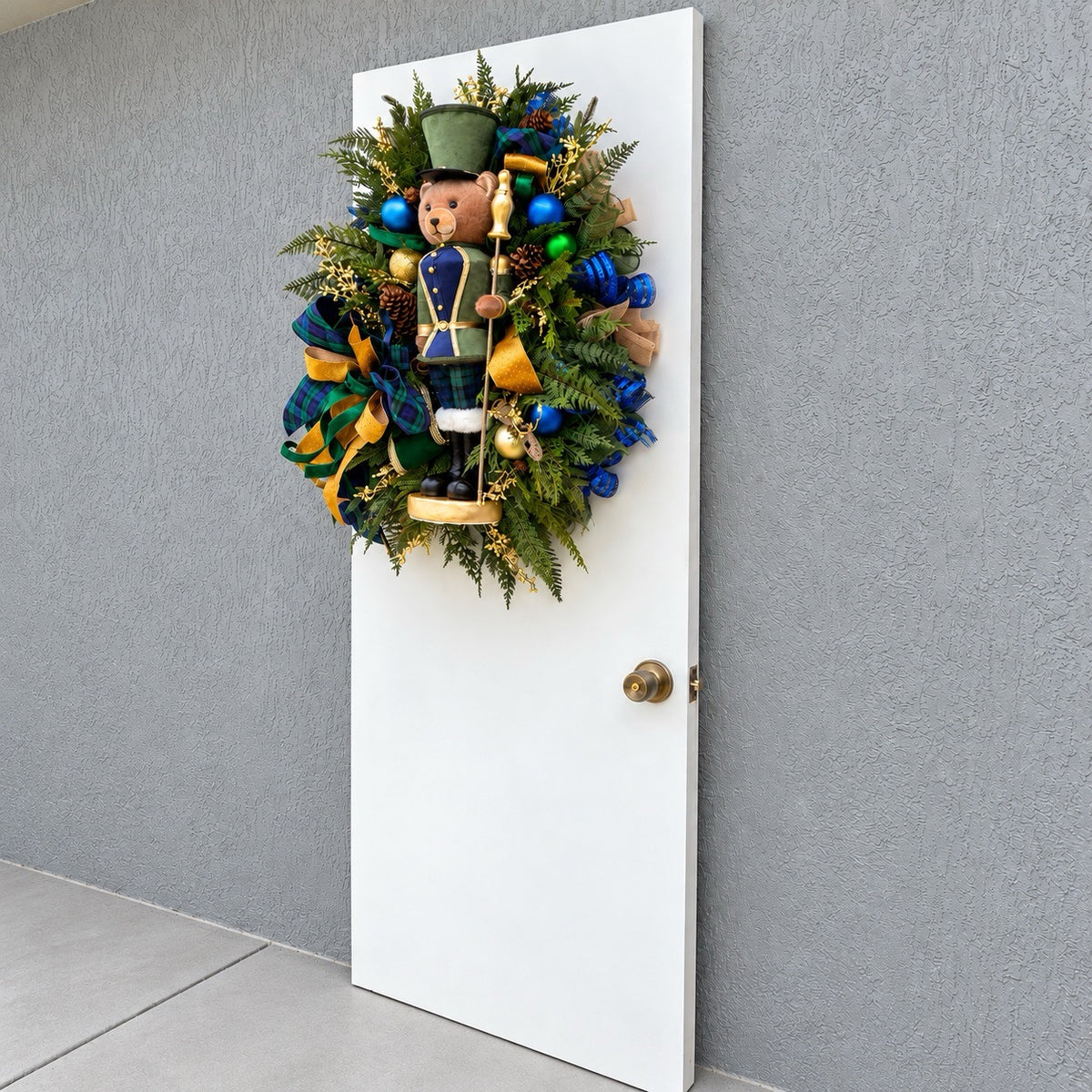 Full view of handmade teddy bear Christmas wreath with evergreen, navy ornaments and gold ribbon.