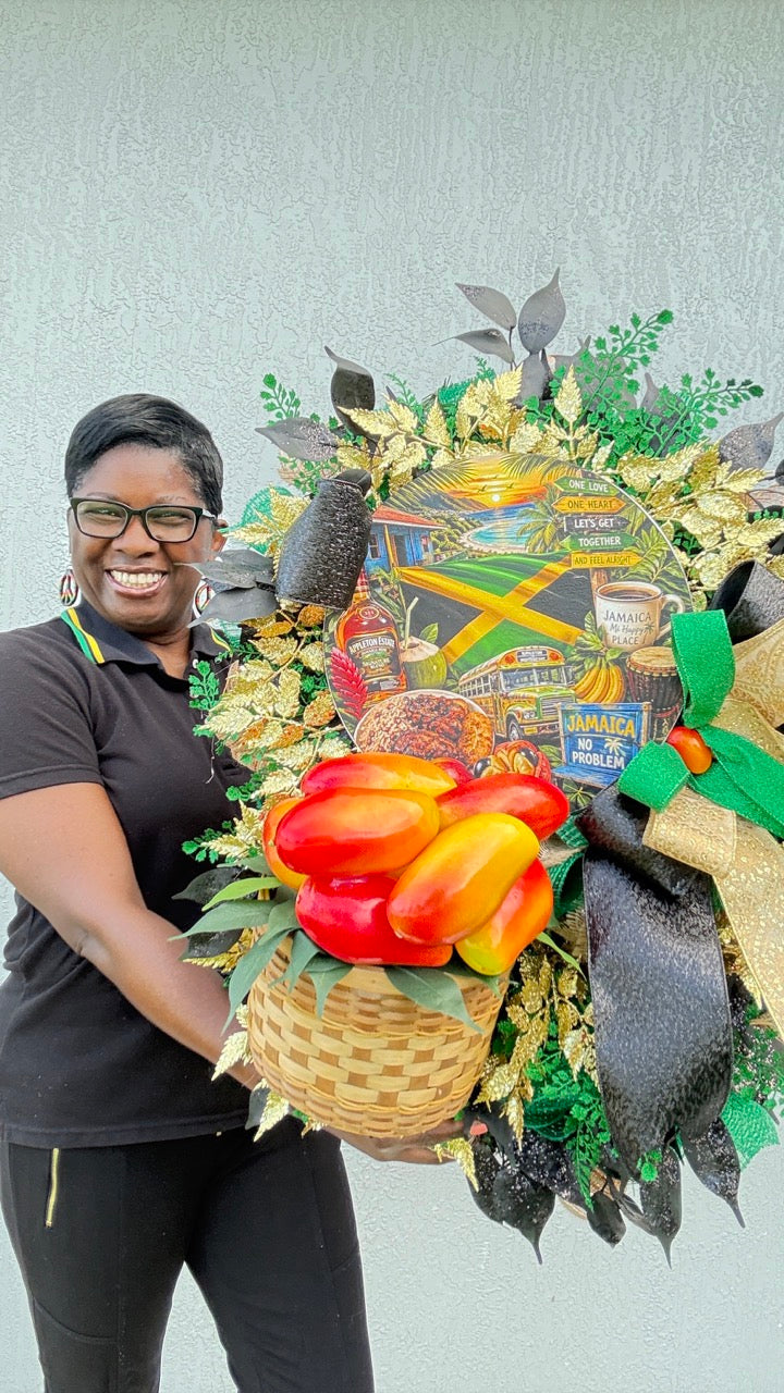 Luxury handmade Jamaica-inspired door wreath featuring green, black, and gold designer ribbons, tropical fruit basket, glittered foliage, and colorful island-themed artwork celebrating Jamaican culture and Caribbean décor.