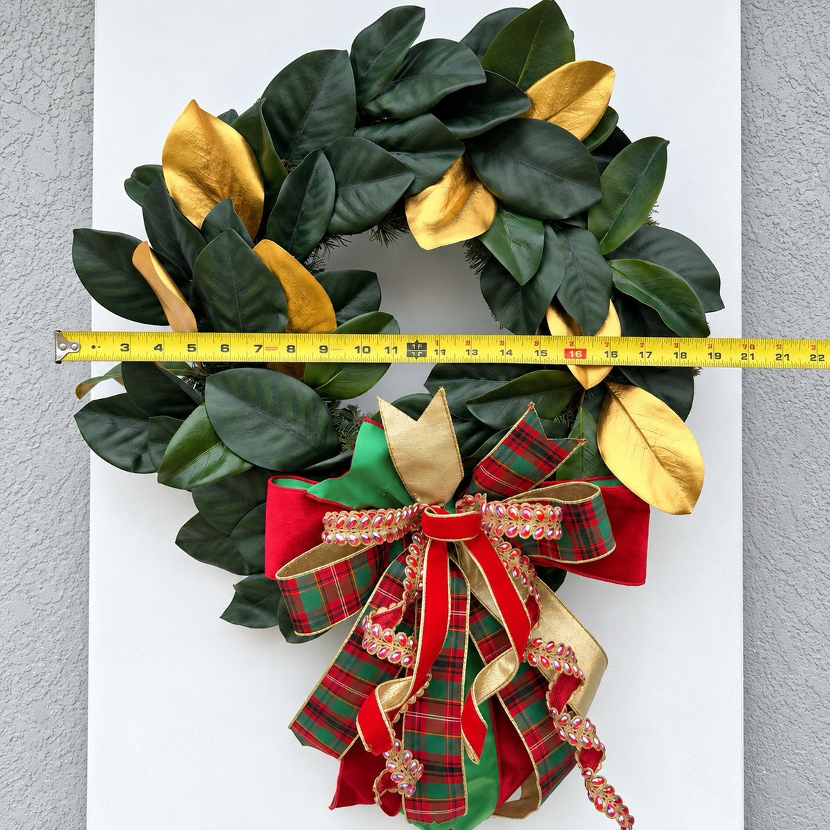 Handmade magnolia Christmas wreath with gold leaves and oversized red green tartan plaid and jeweled holiday bow