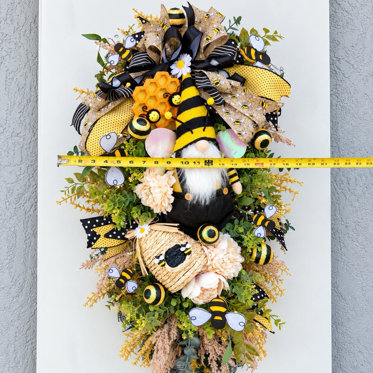 Handmade Queen Bee Manor wreath featuring a bee gnome, woven beehive, yellow and black designer bow, honeycomb accents, florals, bees, and lush greenery.