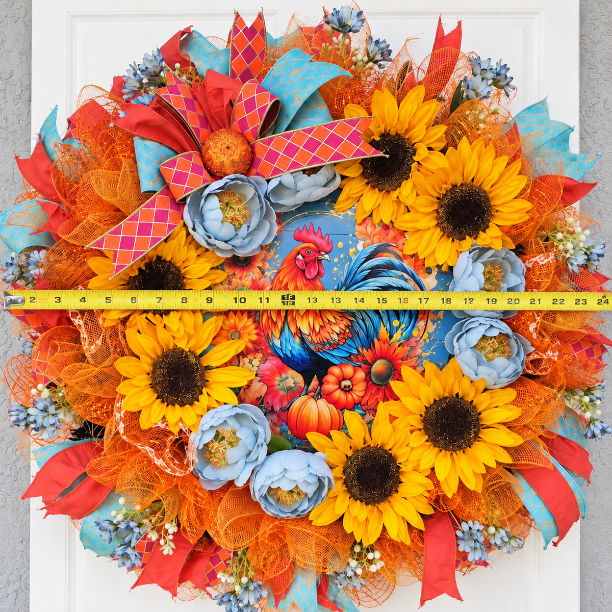 Handmade fall rooster wreath featuring vibrant yellow sunflowers, dusty blue flowers, orange deco mesh, coral and turquoise ribbons, and a colorful rooster centerpiece. A full farmhouse-style autumn wreath displayed on a white front door.