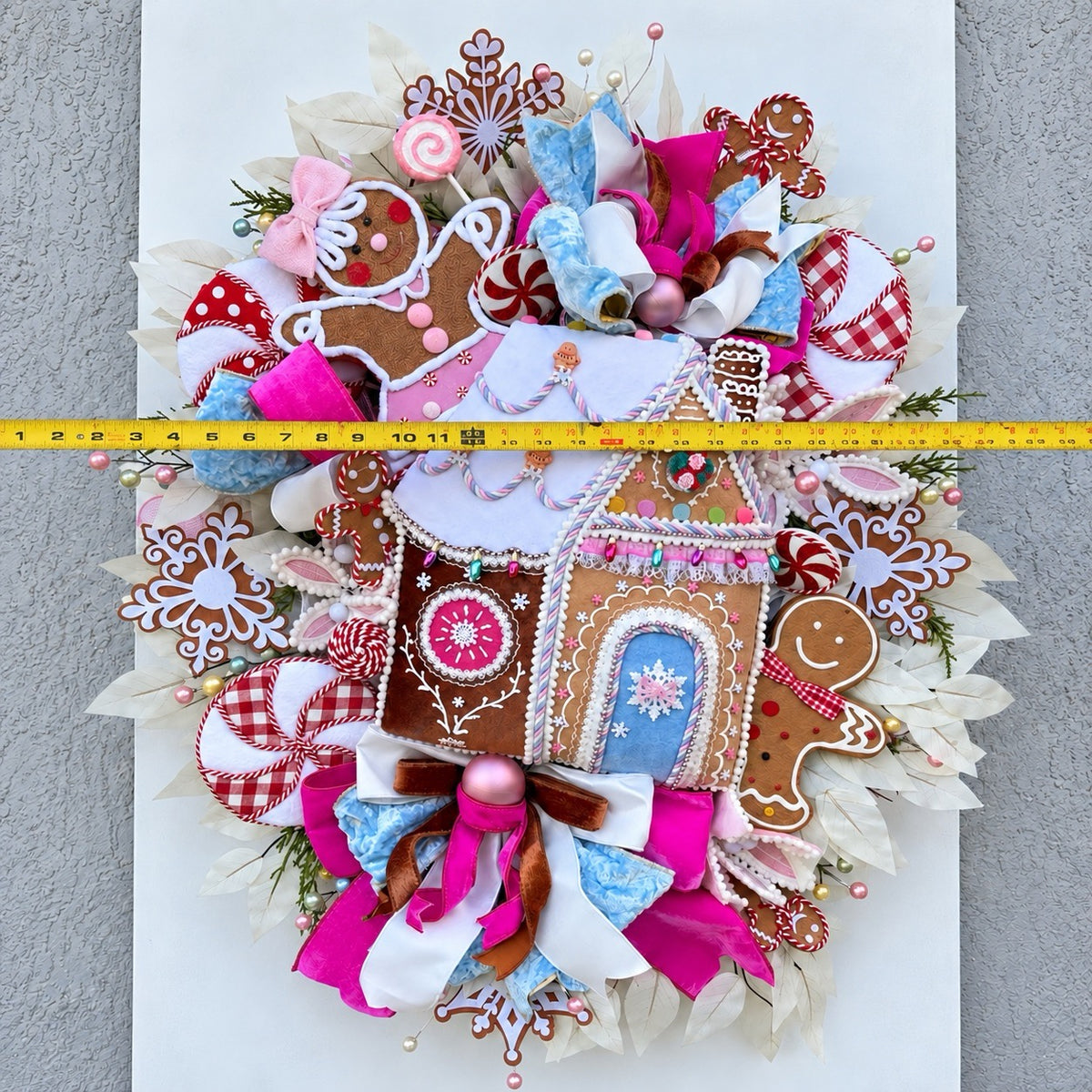 Sugarplum Gingerbread Cottage Christmas Wreath with pastel gingerbread house, pink and blue bows, poinsettias and Norfolk fir greenery.