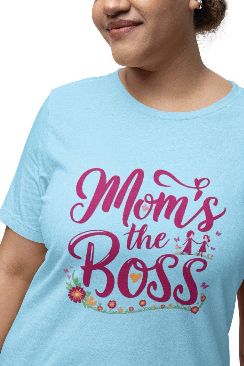 Woman wearing a blue T-shirt with bold pink script reading “Mom’s the Boss,” decorated with flowers, hearts, and a small illustration of a mother and child.