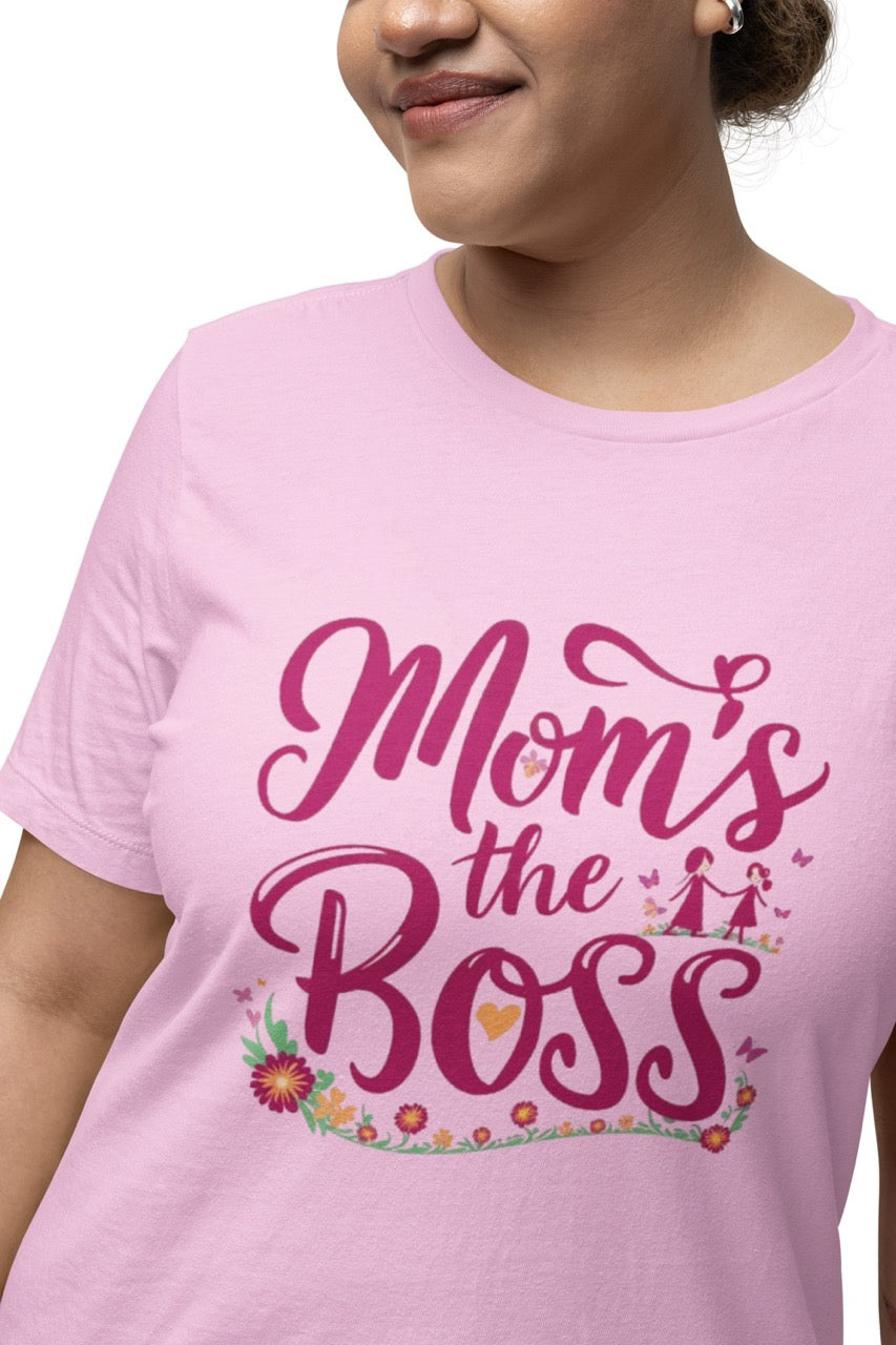 Woman wearing a pink T-shirt with bold pink script reading “Mom’s the Boss,” decorated with flowers, hearts, and a small illustration of a mother and child.