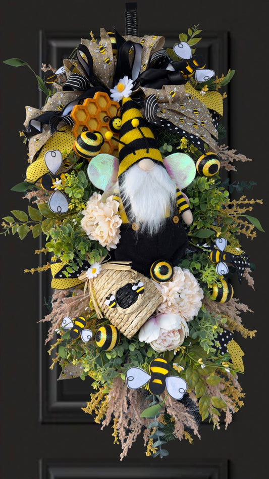 Luxury bee-themed door swag featuring a whimsical bee gnome, honeycomb decoration, beehive accent, premium black and yellow ribbons, lush greenery, cream florals, and sparkling bee embellishments, perfect for spring and summer front door décor.