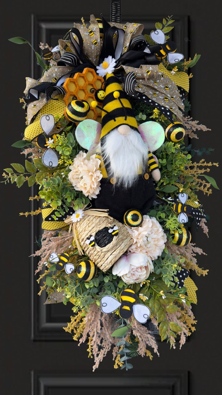 Luxury bee-themed door swag featuring a whimsical bee gnome, honeycomb decoration, beehive accent, premium black and yellow ribbons, lush greenery, cream florals, and sparkling bee embellishments, perfect for spring and summer front door décor.