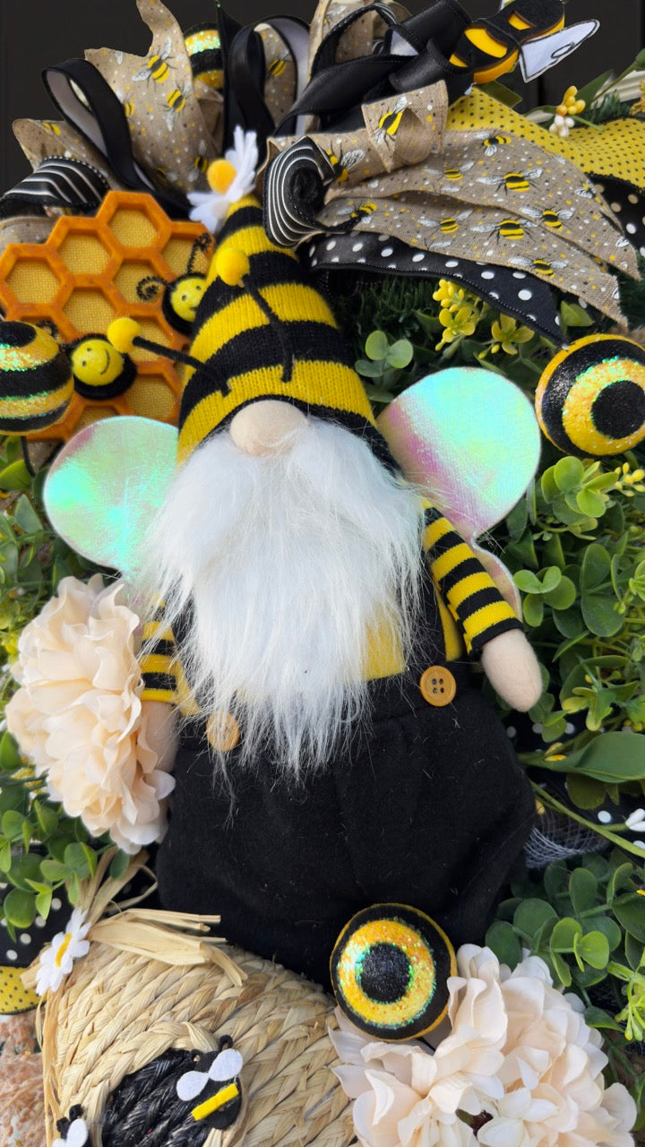 Luxury bee-themed door swag featuring a whimsical bee gnome, honeycomb decoration, beehive accent, premium black and yellow ribbons, lush greenery, cream florals, and sparkling bee embellishments, perfect for spring and summer front door décor.