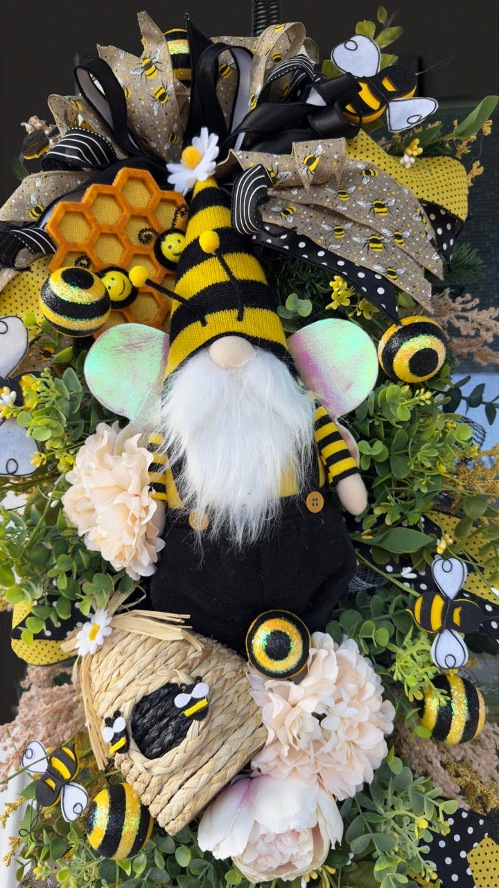 Luxury bee-themed door swag featuring a whimsical bee gnome, honeycomb decoration, beehive accent, premium black and yellow ribbons, lush greenery, cream florals, and sparkling bee embellishments, perfect for spring and summer front door décor.