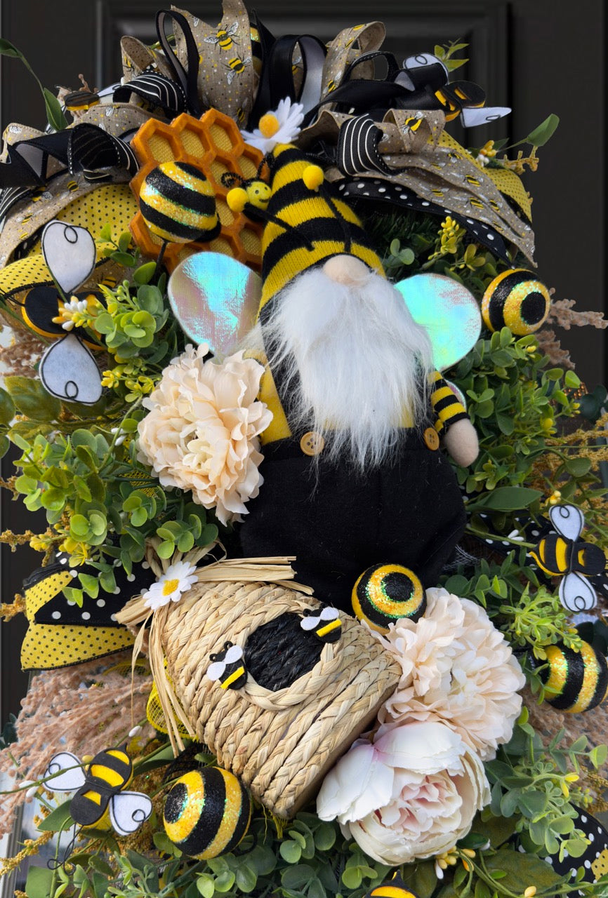 Luxury bee-themed door swag featuring a whimsical bee gnome, honeycomb decoration, beehive accent, premium black and yellow ribbons, lush greenery, cream florals, and sparkling bee embellishments, perfect for spring and summer front door décor.