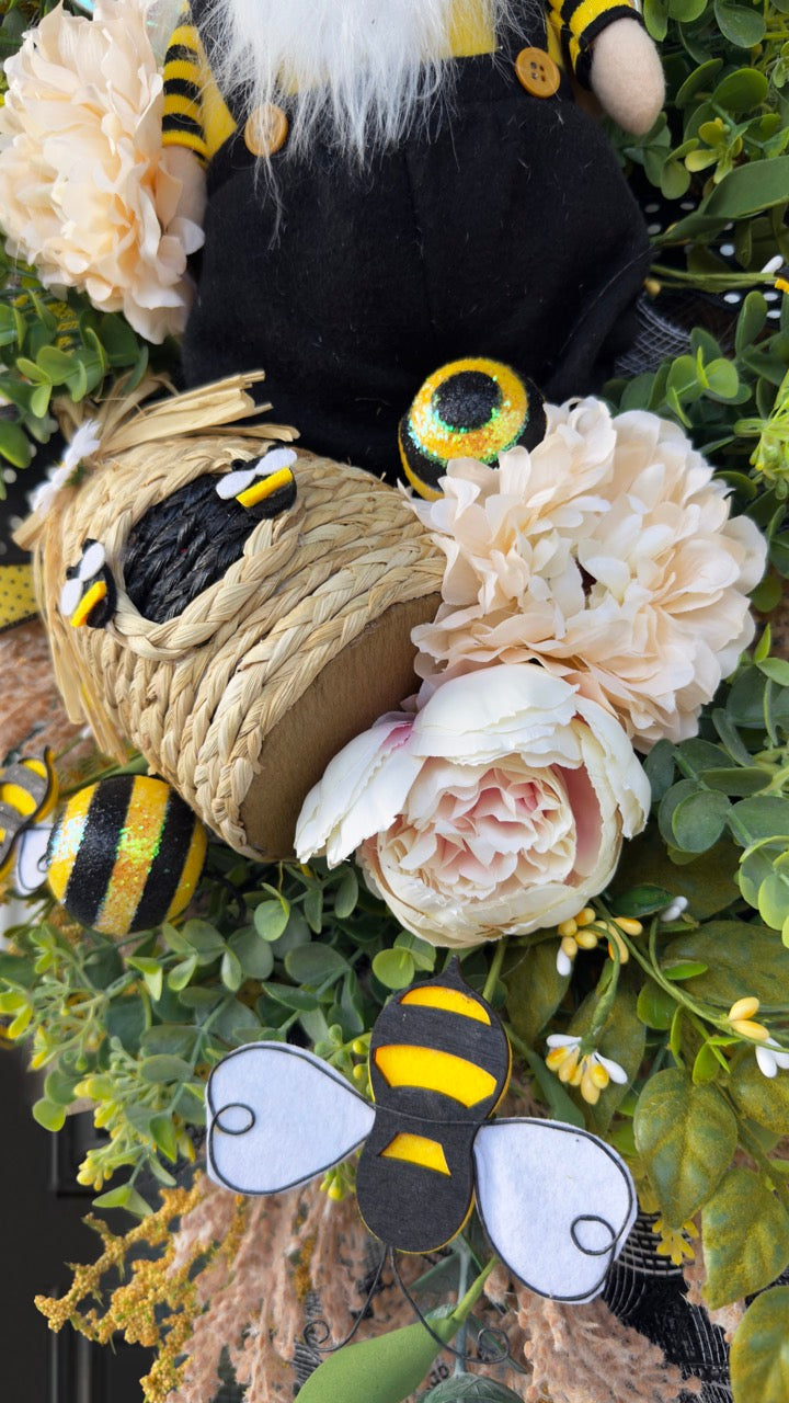 Luxury bee-themed door swag featuring a whimsical bee gnome, honeycomb decoration, beehive accent, premium black and yellow ribbons, lush greenery, cream florals, and sparkling bee embellishments, perfect for spring and summer front door décor.