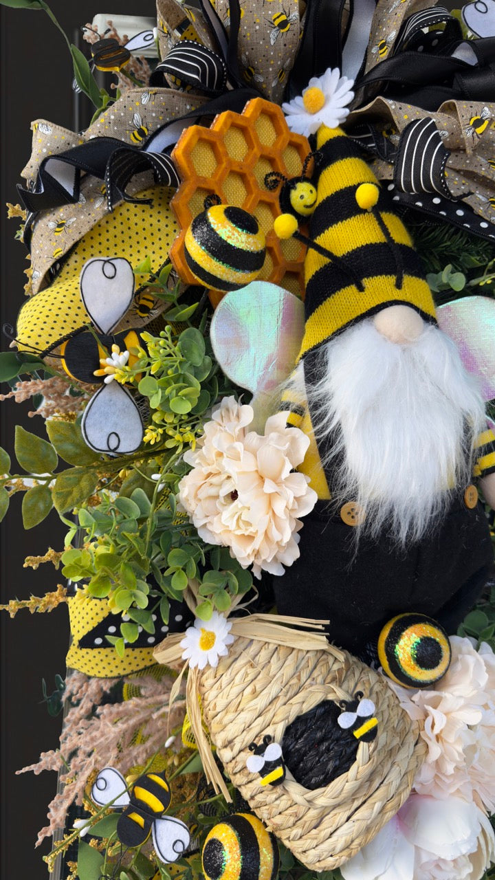 Luxury bee-themed door swag featuring a whimsical bee gnome, honeycomb decoration, beehive accent, premium black and yellow ribbons, lush greenery, cream florals, and sparkling bee embellishments, perfect for spring and summer front door décor.