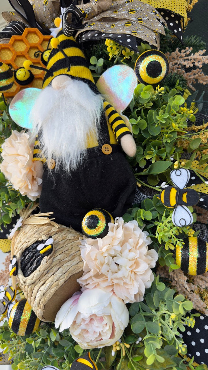Luxury bee-themed door swag featuring a whimsical bee gnome, honeycomb decoration, beehive accent, premium black and yellow ribbons, lush greenery, cream florals, and sparkling bee embellishments, perfect for spring and summer front door décor.