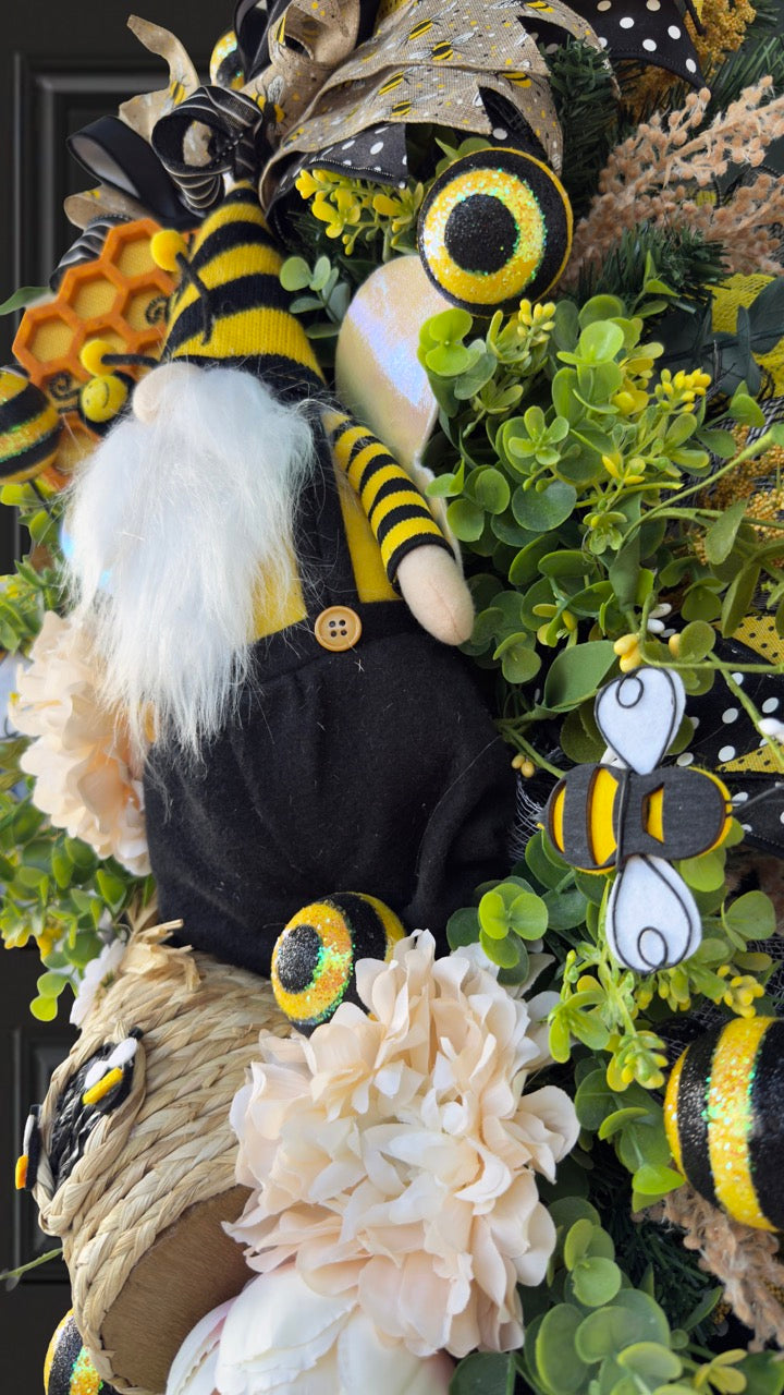 Luxury bee-themed door swag featuring a whimsical bee gnome, honeycomb decoration, beehive accent, premium black and yellow ribbons, lush greenery, cream florals, and sparkling bee embellishments, perfect for spring and summer front door décor.