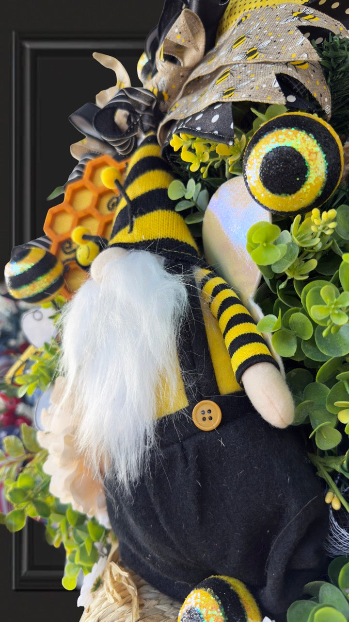 Luxury bee-themed door swag featuring a whimsical bee gnome, honeycomb decoration, beehive accent, premium black and yellow ribbons, lush greenery, cream florals, and sparkling bee embellishments, perfect for spring and summer front door décor.