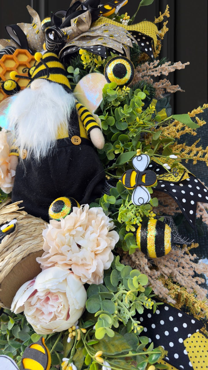 Luxury bee-themed door swag featuring a whimsical bee gnome, honeycomb decoration, beehive accent, premium black and yellow ribbons, lush greenery, cream florals, and sparkling bee embellishments, perfect for spring and summer front door décor.