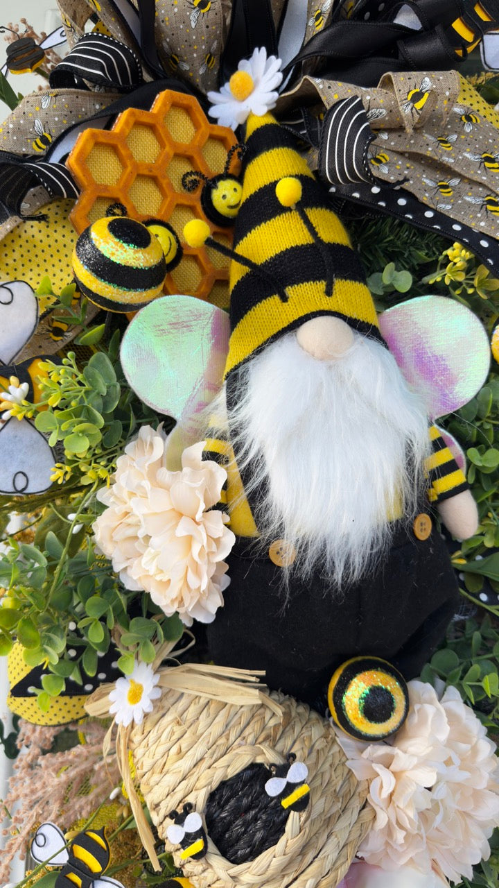 Luxury bee-themed door swag featuring a whimsical bee gnome, honeycomb decoration, beehive accent, premium black and yellow ribbons, lush greenery, cream florals, and sparkling bee embellishments, perfect for spring and summer front door décor.