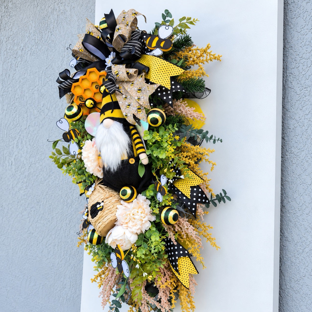 Handmade Queen Bee Manor wreath featuring a bee gnome, woven beehive, yellow and black designer bow, honeycomb accents, florals, bees, and lush greenery.