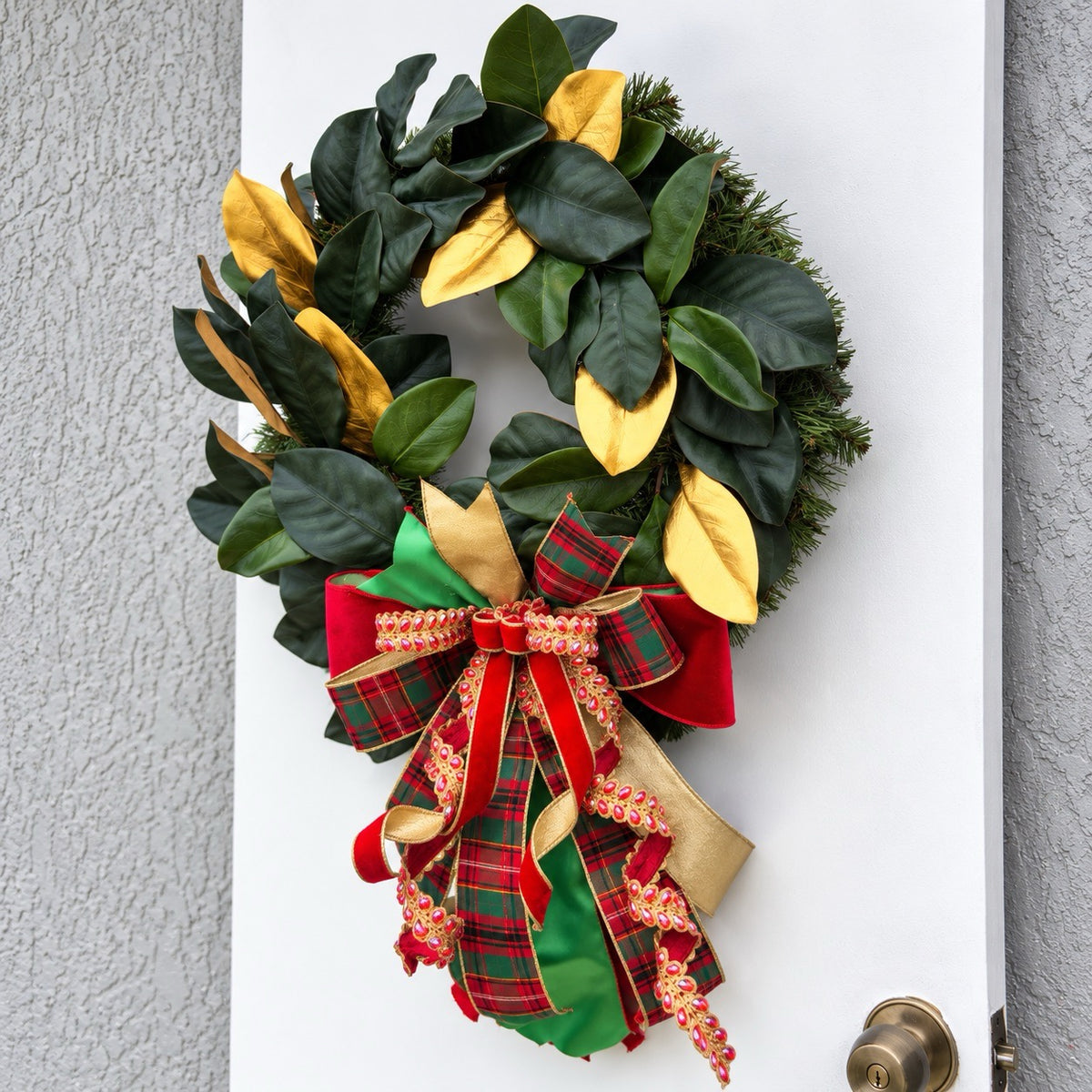 Handmade magnolia Christmas wreath with gold leaves and oversized red green tartan plaid and jeweled holiday bow