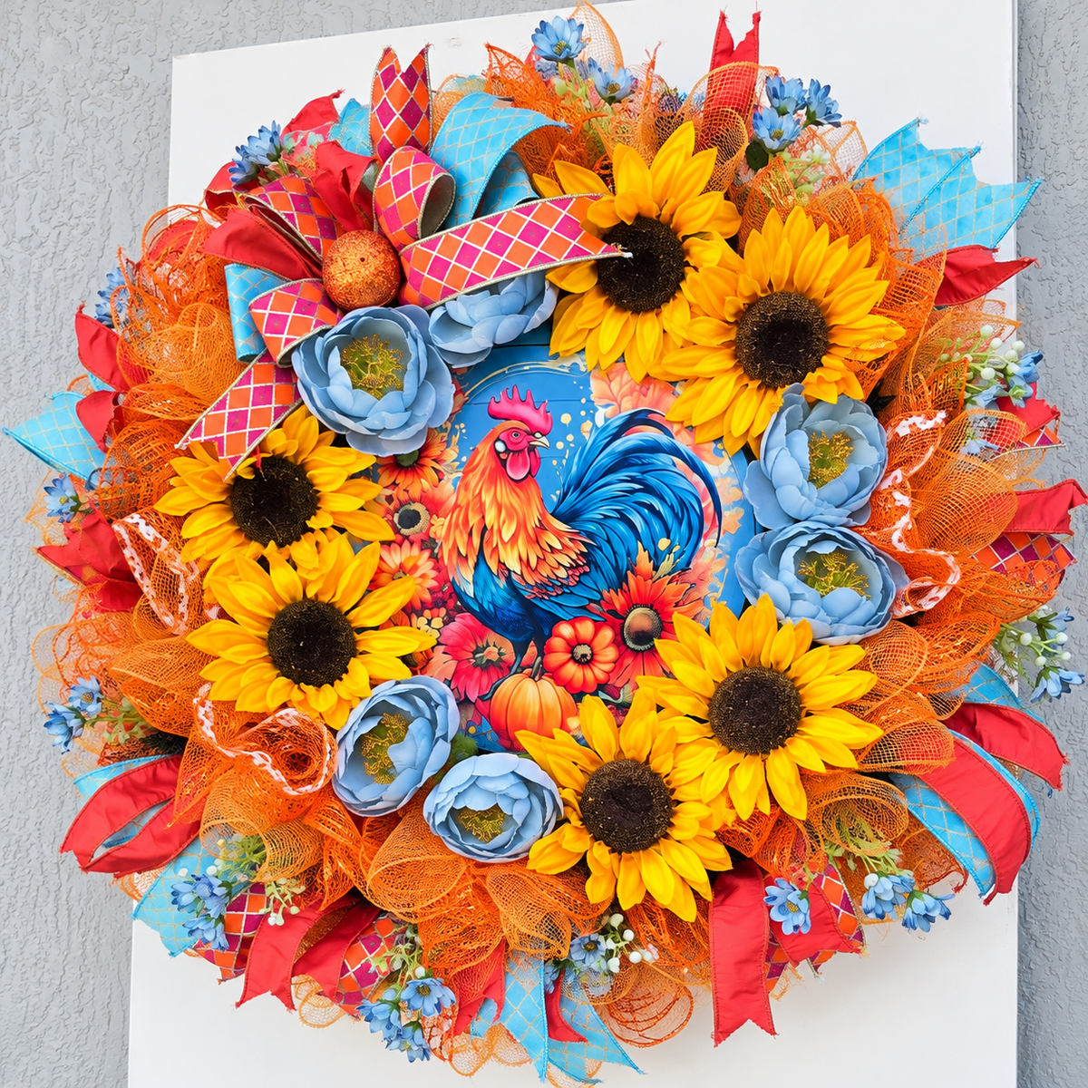 Handmade fall rooster wreath featuring vibrant yellow sunflowers, dusty blue flowers, orange deco mesh, coral and turquoise ribbons, and a colorful rooster centerpiece. A full farmhouse-style autumn wreath displayed on a white front door.