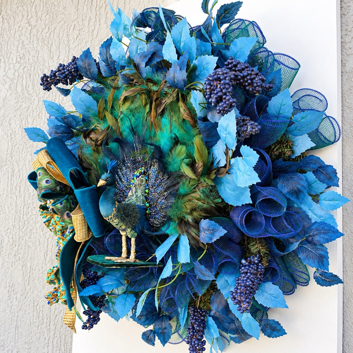 Right-angle view of luxury peacock wreath featuring textured leaves and turquoise feathers.