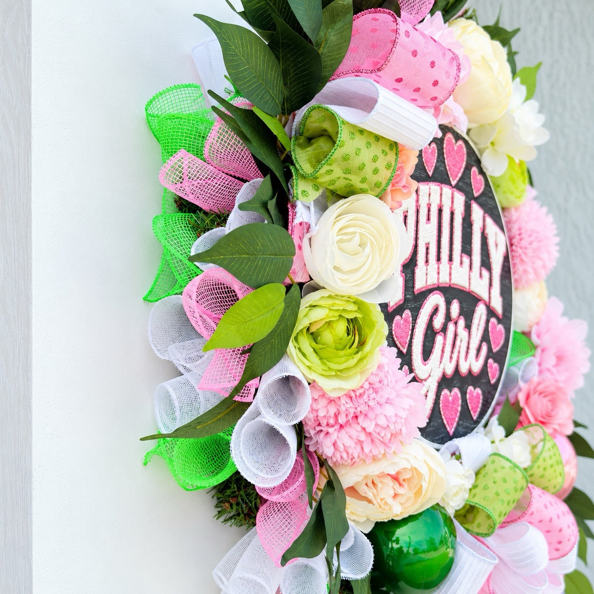 Left-angle view of handmade Philly Girl wreath showing layered greenery, pink flowers, ivory blooms, and decorative ribbon details.