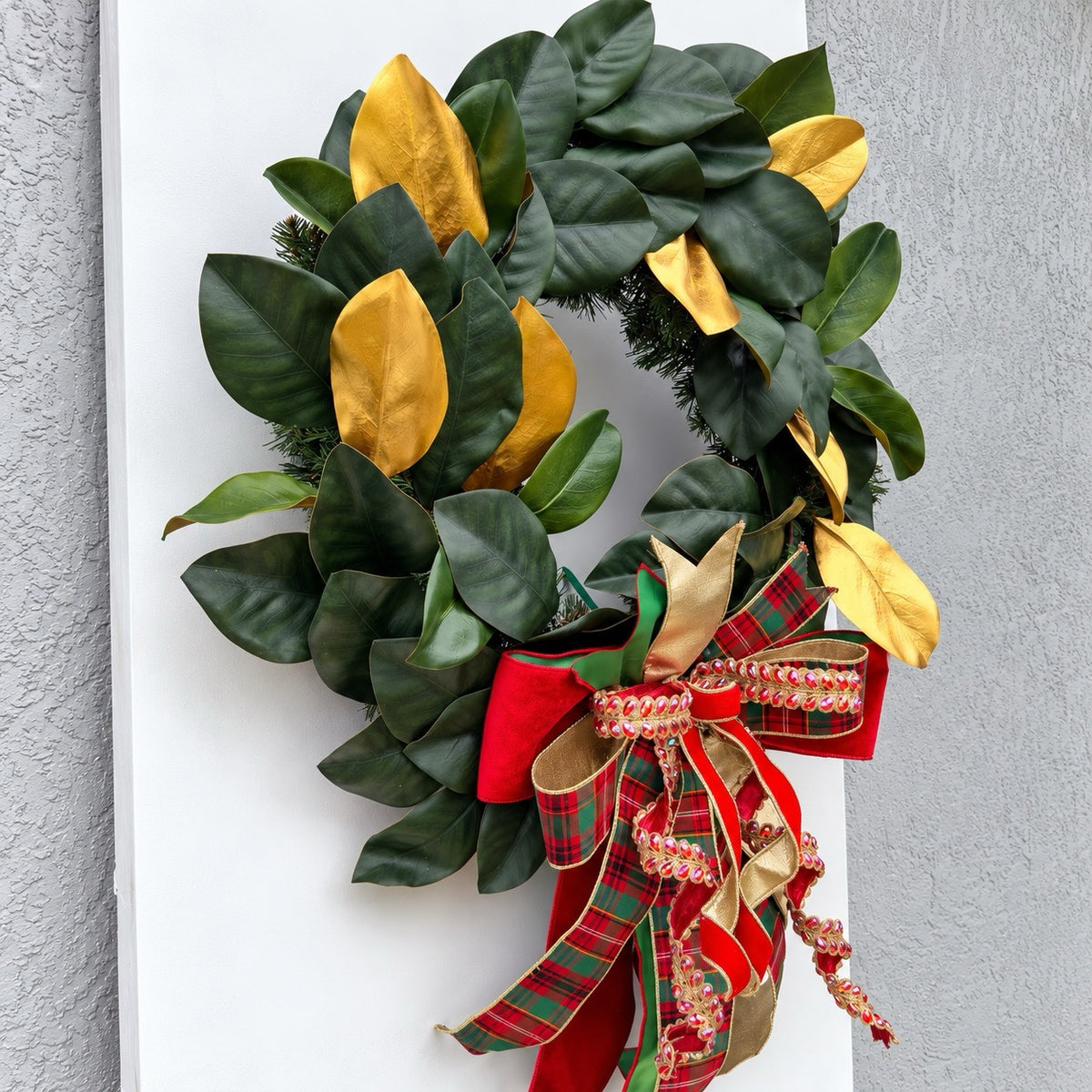 Handmade magnolia Christmas wreath with gold leaves and oversized red green tartan plaid and jeweled holiday bow