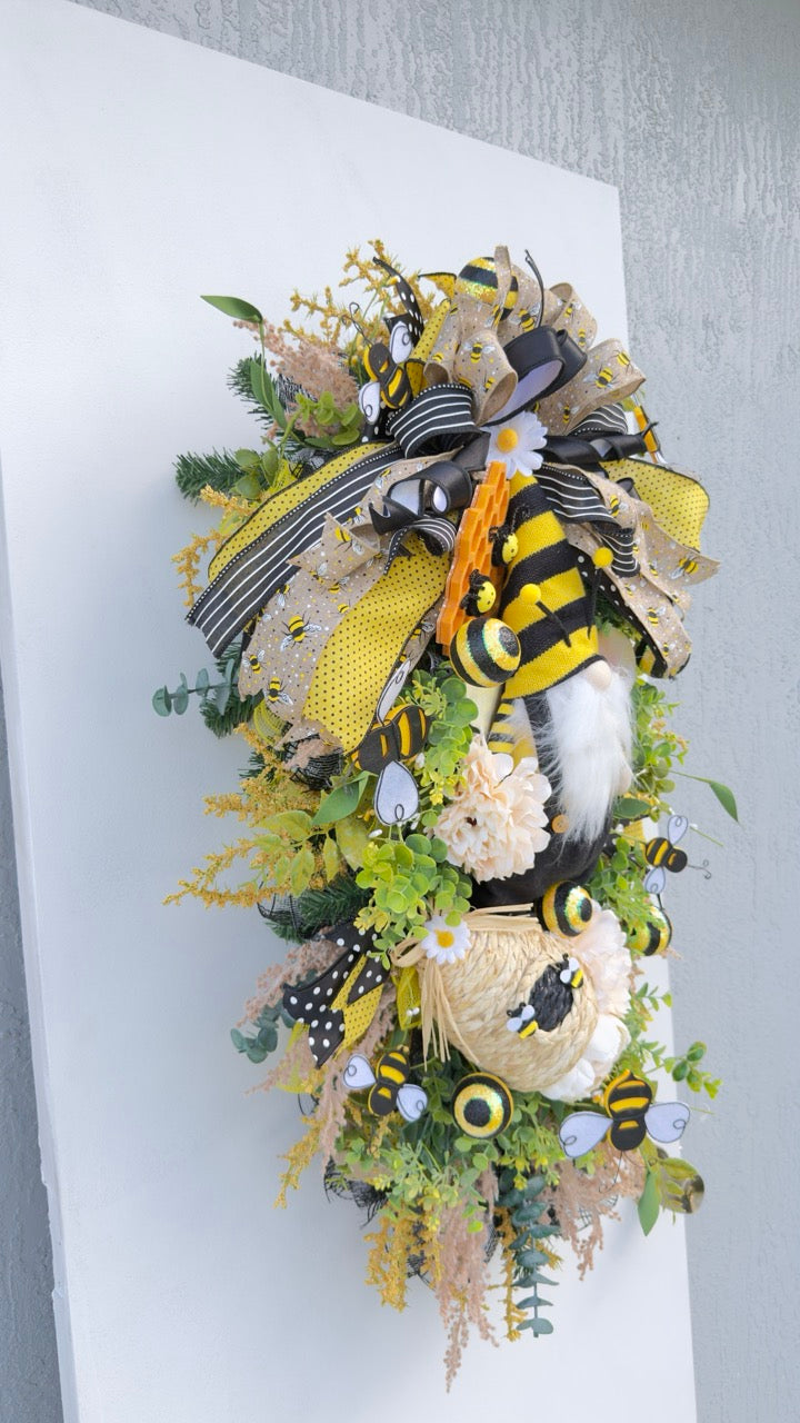 Handmade Queen Bee Manor wreath featuring a bee gnome, woven beehive, yellow and black designer bow, honeycomb accents, florals, bees, and lush greenery.