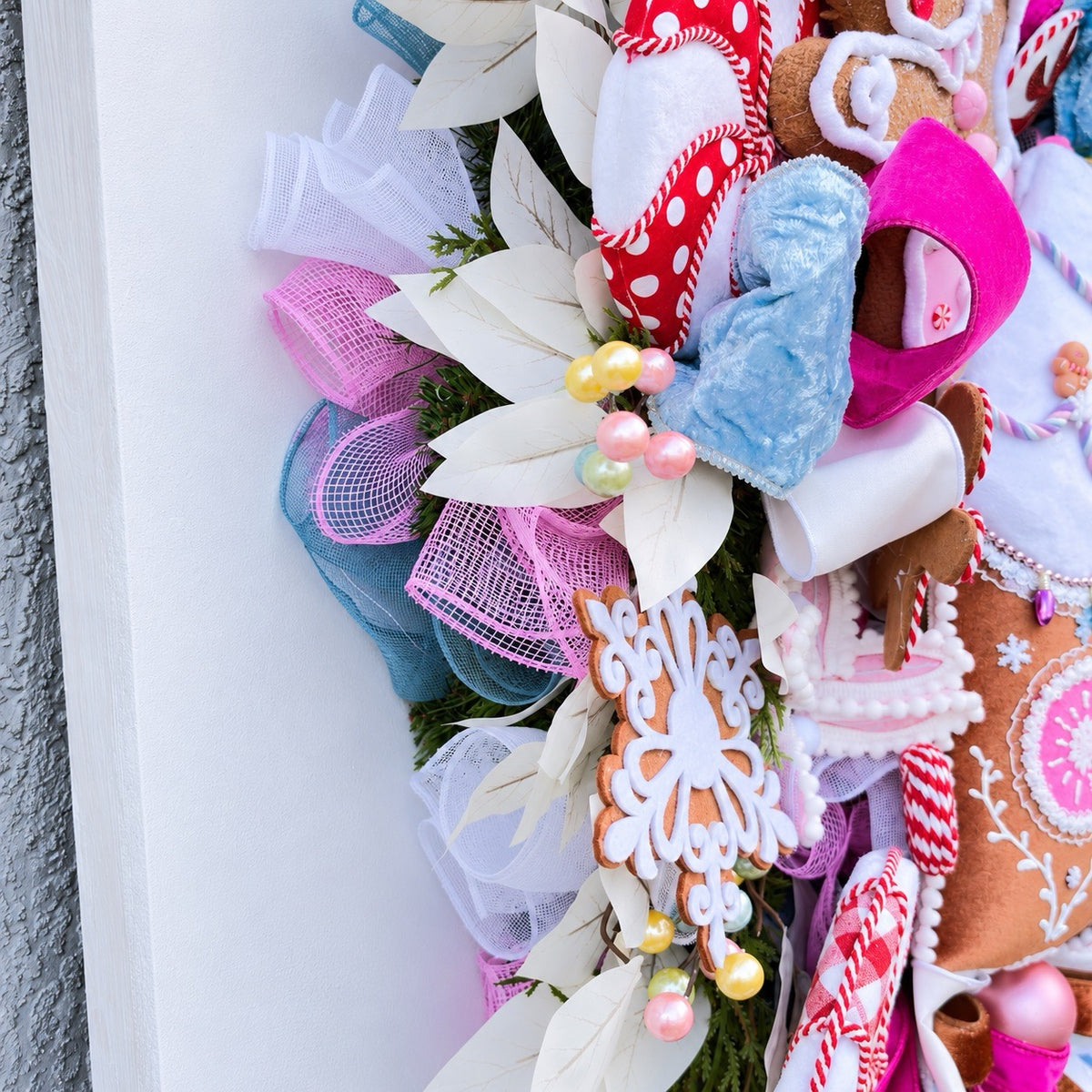 Sugarplum Gingerbread Cottage Christmas Wreath with pastel gingerbread house, pink and blue bows, poinsettias and Norfolk fir greenery.