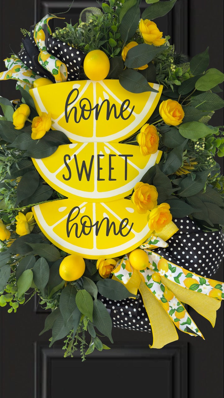 Handmade summer lemon wreath with stacked lemon slice signs reading ‘Home Sweet Home,’ decorated with yellow flowers, faux lemons, greenery, and polka‑dot and lemon‑print ribbons