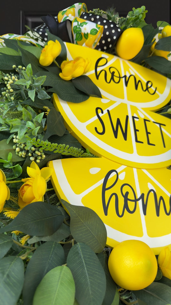 Handmade summer lemon wreath with stacked lemon slice signs reading ‘Home Sweet Home,’ decorated with yellow flowers, faux lemons, greenery, and polka‑dot and lemon‑print ribbons