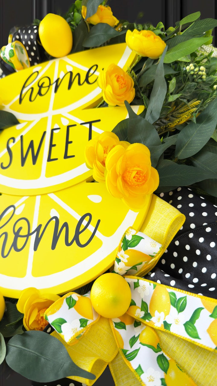 Handmade summer lemon wreath with stacked lemon slice signs reading ‘Home Sweet Home,’ decorated with yellow flowers, faux lemons, greenery, and polka‑dot and lemon‑print ribbons