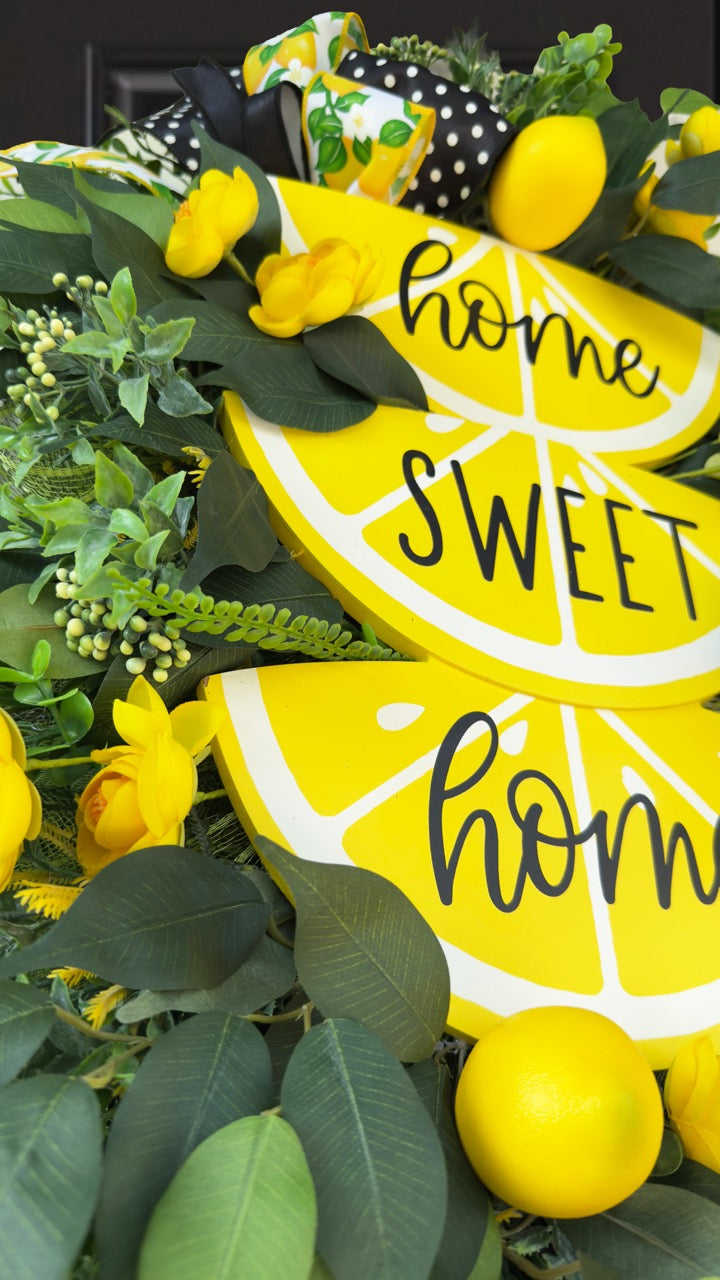 Handmade summer lemon wreath with stacked lemon slice signs reading ‘Home Sweet Home,’ decorated with yellow flowers, faux lemons, greenery, and polka‑dot and lemon‑print ribbons