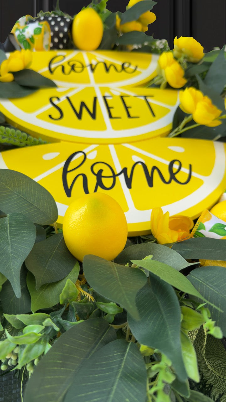 Handmade summer lemon wreath with stacked lemon slice signs reading ‘Home Sweet Home,’ decorated with yellow flowers, faux lemons, greenery, and polka‑dot and lemon‑print ribbons
