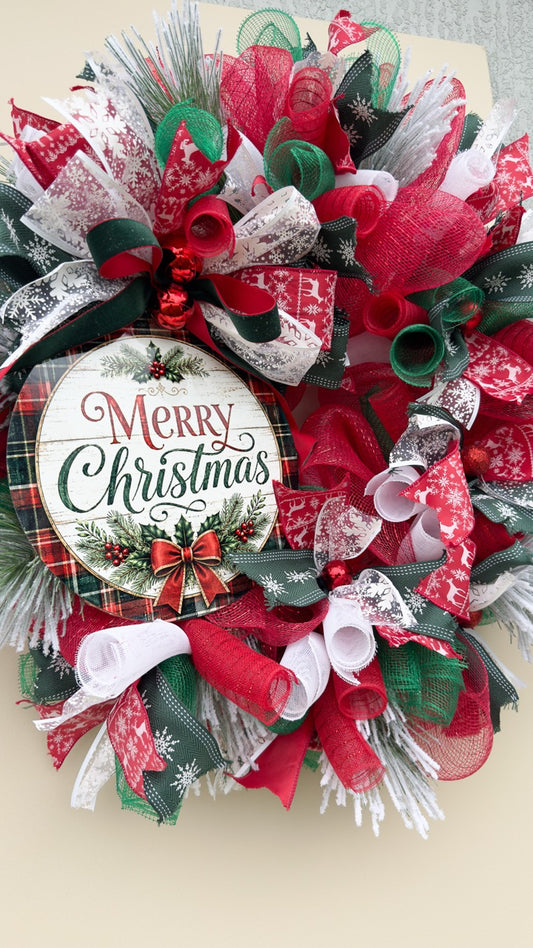 Traditional plaid and pine Merry Christmas wreath with red, green and white ribbon, decorative mesh, frosted greenery and Christmas sign on a front door