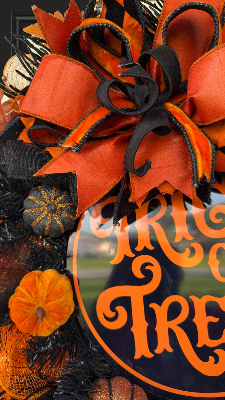 Black and orange Halloween wreath with layered mesh, designer ribbons, fall leaves, glitter pumpkins, and a round “Trick or Treat” sign.