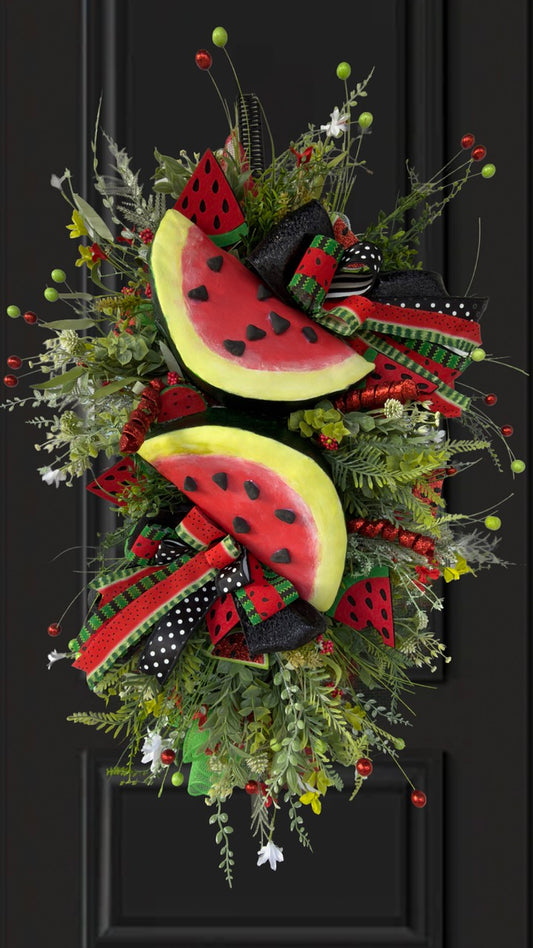 Handmade luxury watermelon summer swag wreath featuring oversized watermelon slices, designer red and green ribbon bows, lush greenery, berry sprays, and whimsical farmhouse accents displayed on a black front door.