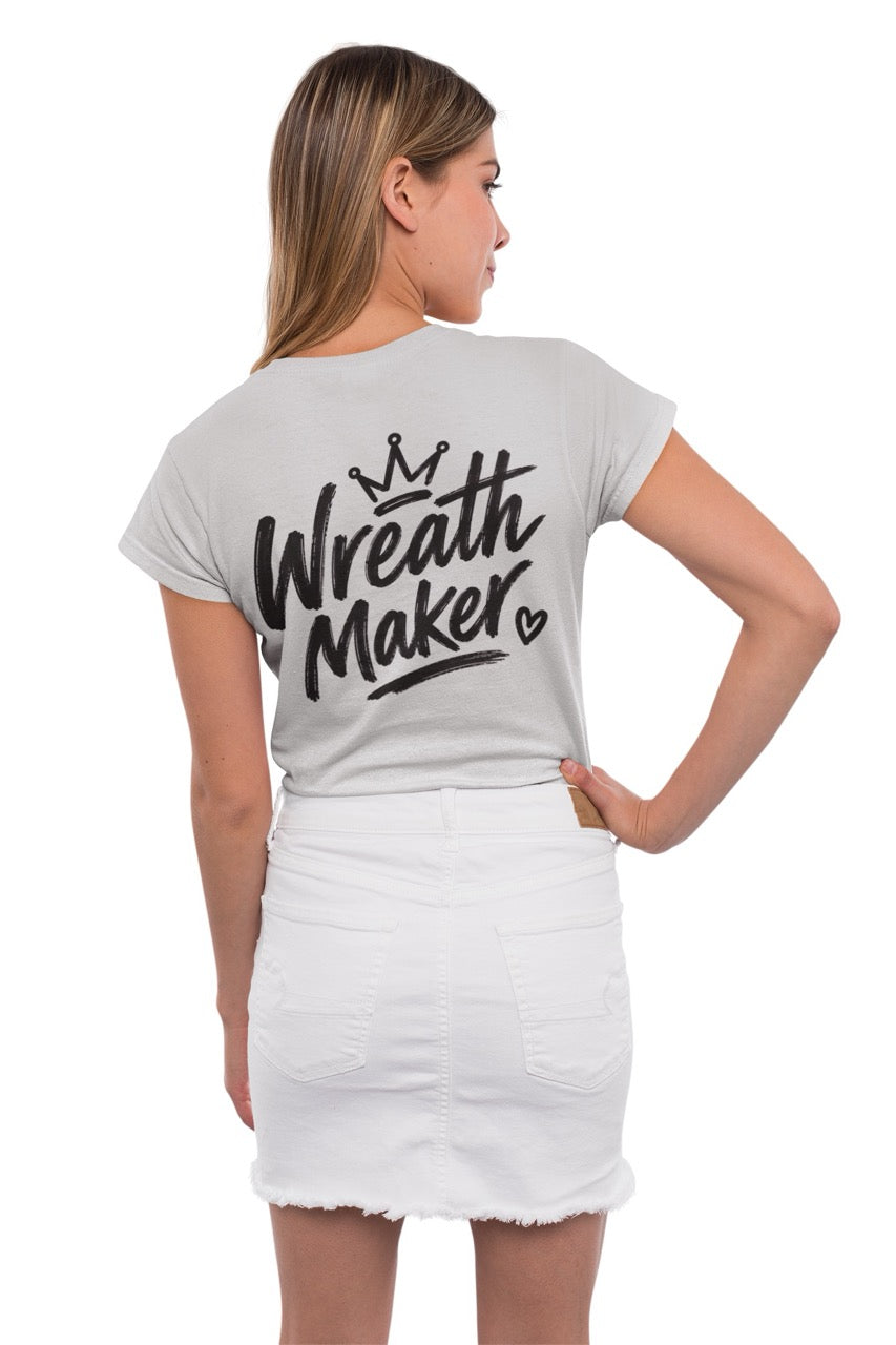 Back view of a t-shirt displaying the words “Wreath Maker” in large brush-style lettering with a crown above and a small heart beside the design. The shirt is available in various colors.