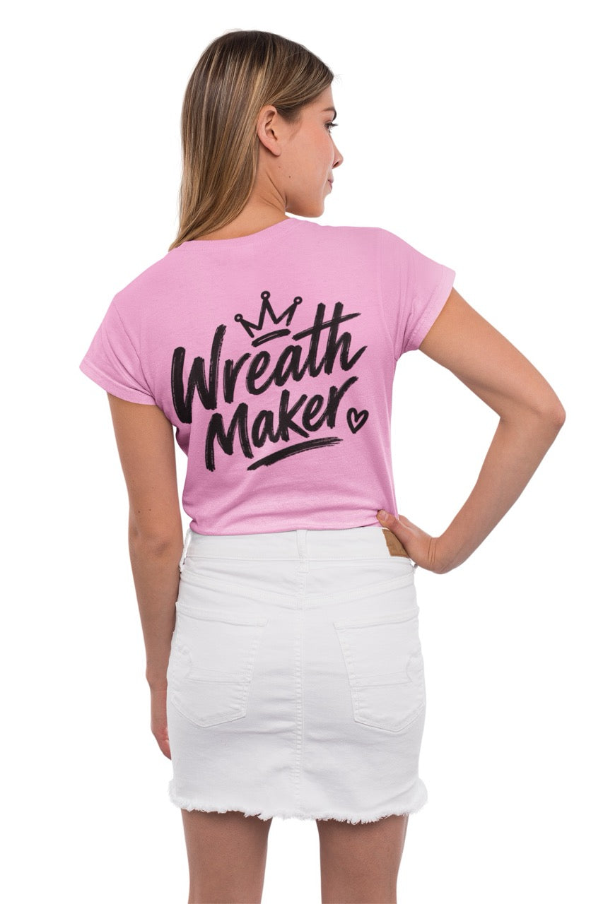 Back view of a t-shirt displaying the words “Wreath Maker” in large brush-style lettering with a crown above and a small heart beside the design. The shirt is available in various colors.